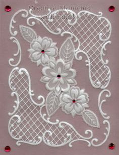 a piece of white lace with flowers and leaves on pink fabric, surrounded by red crystals