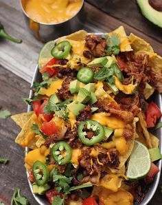 nachos with meat, cheese and vegetables in a metal dish on a wooden table