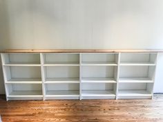 an empty white bookcase with wooden shelves on the floor in front of a wall