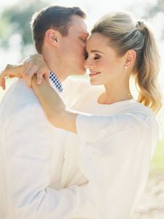 a man and woman standing next to each other near the ocean with their arms around each other