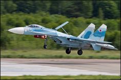 a blue fighter jet taking off from an airport runway with trees in the back ground