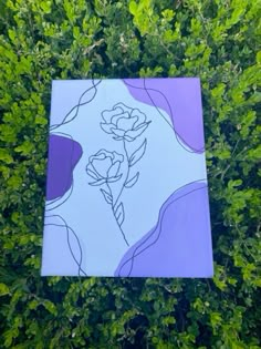 a purple and white painting sitting on top of a green plant covered in lots of leaves