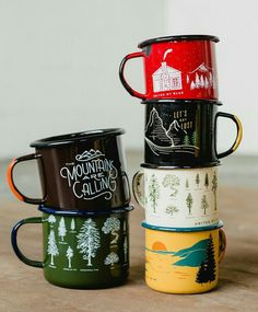 four coffee mugs stacked on top of each other with mountains and trees painted on them