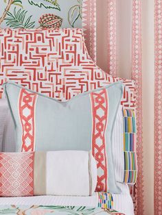 a bed topped with lots of pillows next to a wall covered in pink and white striped curtains