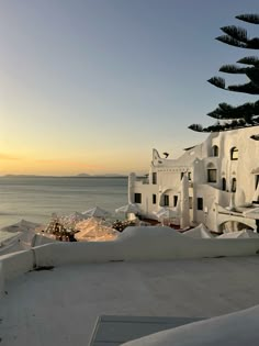 the sun is setting over an old building by the ocean