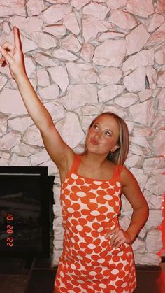 a woman standing in front of a stone wall holding her arms up to the air