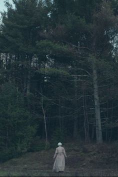 a woman in a white dress is walking through the woods