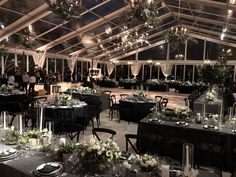 a banquet hall with tables and chairs set up for an event at night, surrounded by greenery and hanging chandeliers