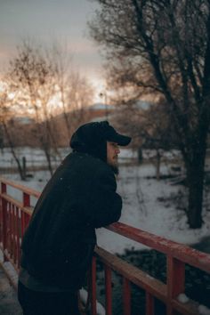 a man standing on a bridge looking at the snow covered ground and trees in the distance