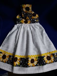 a white dress with sunflowers on it is sitting on a blue cloth background