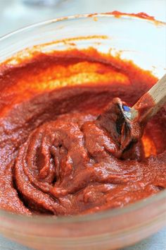 a wooden spoon mixing red sauce in a glass bowl