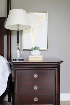 a nightstand with a lamp on top of it next to a bed and a painting