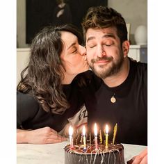 a man and woman kissing while sitting in front of a cake with candles on it