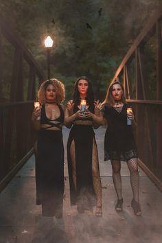 three women standing on a bridge holding candles