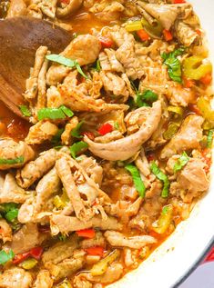 a bowl filled with chicken and vegetables next to a wooden spoon