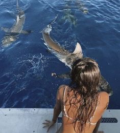 a woman sitting on the side of a boat looking at some sharks in the water