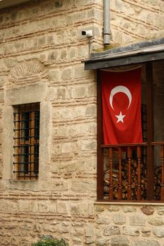 a red flag hanging from the side of a brick building next to a window with bars on it