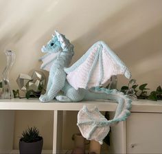 a crocheted dragon sitting on top of a shelf next to a potted plant