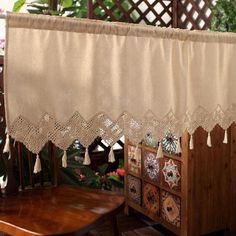 a wooden table sitting under a window covered by a white valance with tassels