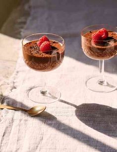 two glasses filled with dessert sitting on top of a white table cloth next to each other