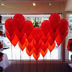 a bunch of red heart shaped balloons in front of a store window with teddy bears on the windowsill