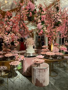 pink flowers are hanging from the ceiling in a room with round tables and stools