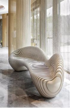 an artisticly designed bench sits in the middle of a room with large windows and sheer curtains