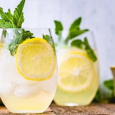 two glasses filled with lemonade and mint sprits on a wooden counter top