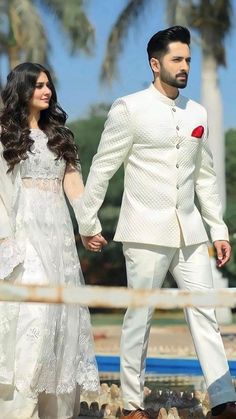 a man and woman dressed in white holding hands