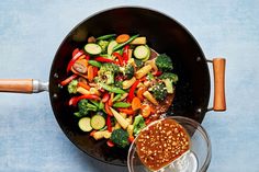 a wok filled with vegetables and seasoning next to a glass of water on a blue surface