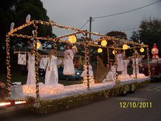 a float with people dressed in white on the back and lights all around it, as well as decorations