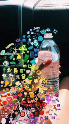 a person holding a bottle of water in their hand with stickers all over it