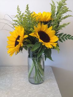 a vase filled with yellow sunflowers on top of a white tablecloth covered table