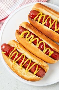 two hotdogs with mustard and ketchup on a plate next to each other