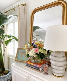 a white dresser topped with lots of flowers and a large gold framed mirror above it