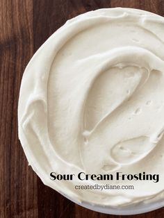 sour cream frosting in a white bowl on top of a wooden table with text overlay that reads sour cream frosting