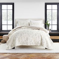 a white bed sitting in a bedroom next to two windows and a rug on top of a wooden floor