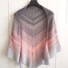 a crocheted shawl hanging on a white wall with a wooden hanger