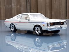 a white model car sitting on top of a glass table next to a wooden fence