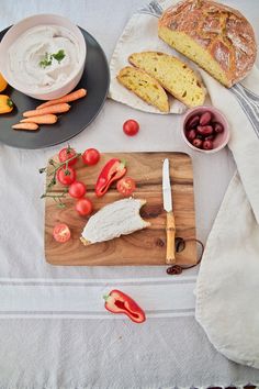 a cutting board with bread, tomatoes, carrots and other food items on it