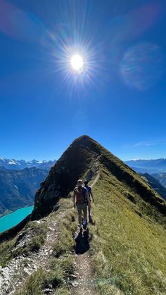 a man hiking up the side of a mountain on a sunny day with blue water in the background