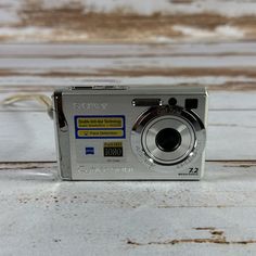 a digital camera sitting on top of a wooden table next to a white wall with peeling paint