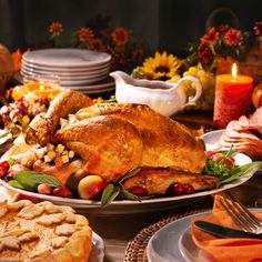 a turkey on a platter surrounded by other thanksgiving foods and dishes with candles in the background