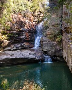 a small waterfall in the middle of a river surrounded by rocks and greenery on either side