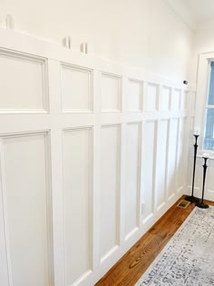 a room with white paneling on the walls and wood floors, along with a rug