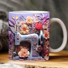 a coffee mug with a sewing machine and flowers painted on the side sitting on a wooden table