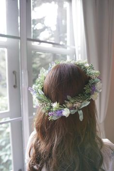 a woman with long hair wearing a wreath of flowers on her head looking out the window