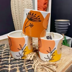 three orange and white cups sitting on top of a wooden table next to a vase