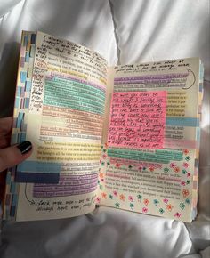 a hand holding an open book with writing on the pages and colorful papers in it