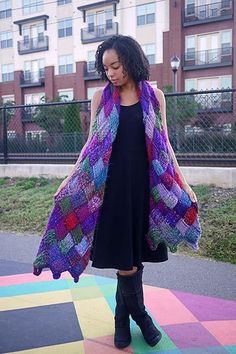 a woman standing in front of a building wearing a multicolored knitted shawl